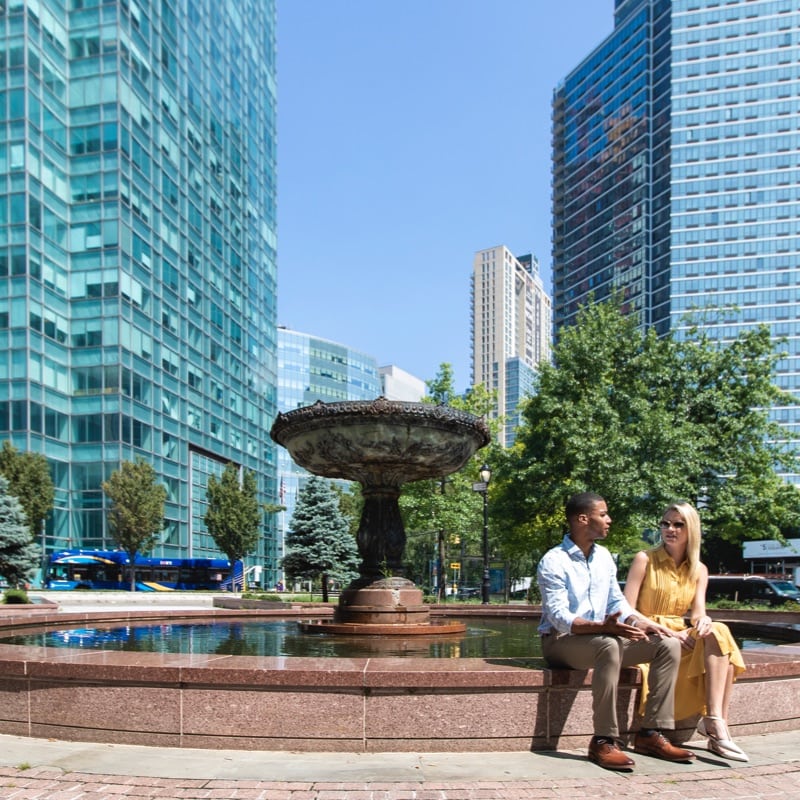 A man and woman sit together and talk on a decorative fountain in a NYC park