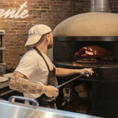 Thumbnail of a chef carefully placing a pizza in a wood-fired oven