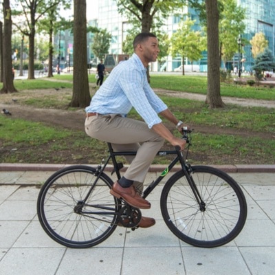 Thumbnail of African-American man in business casual attire riding a bike through a city park