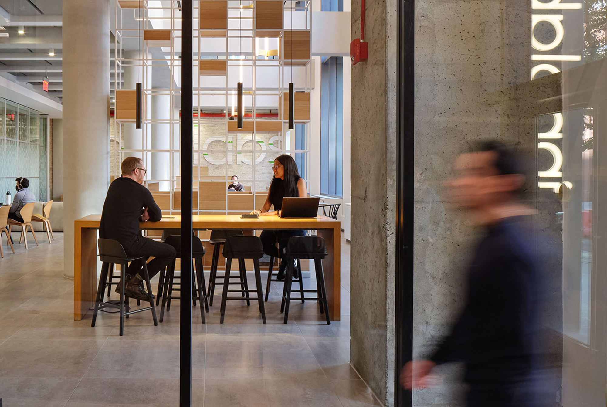 Presenter talking to a crowd in an open conference room with 6 wall-mounted TV's